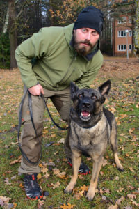 Hundföraren Fredrik står med sin polishund Magda utomhus. De ser båda lite aggressiva ut. De visar hur Magda tränar på personskydd. 