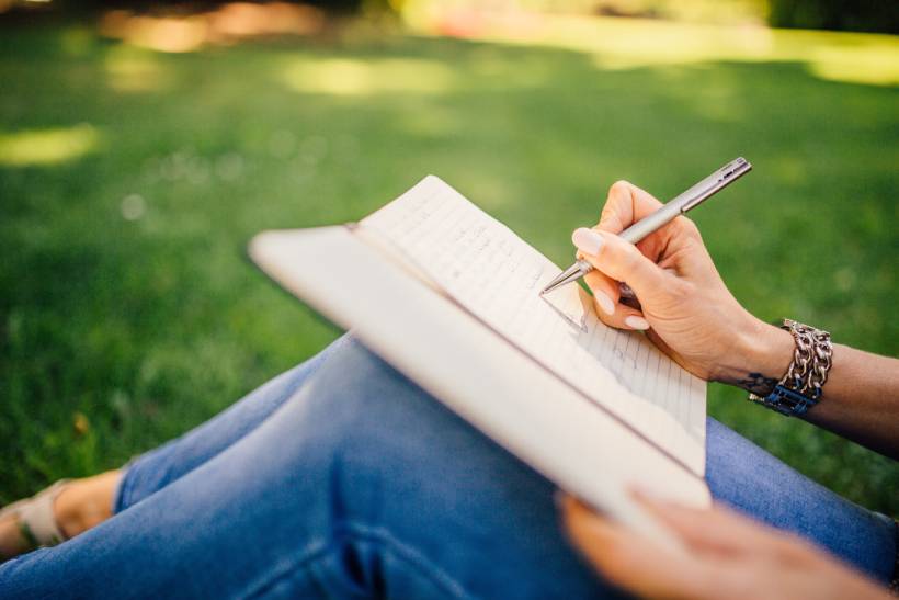 En kvinna som sitter och skriver för hand i en anteckningsbok.