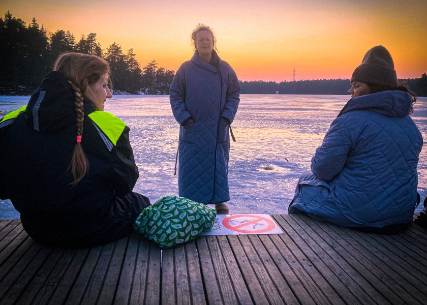 Elise står på isen framför Berit och Sophia som sitter på bryggan. 