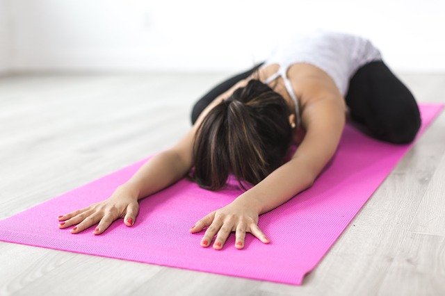 Kvinna i yogaposition på rosa yogamatta som ligger på golvet